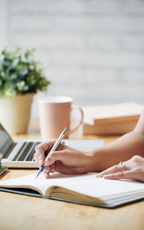 unrecognizable-woman-sitting-desk-indoors-writing-planner